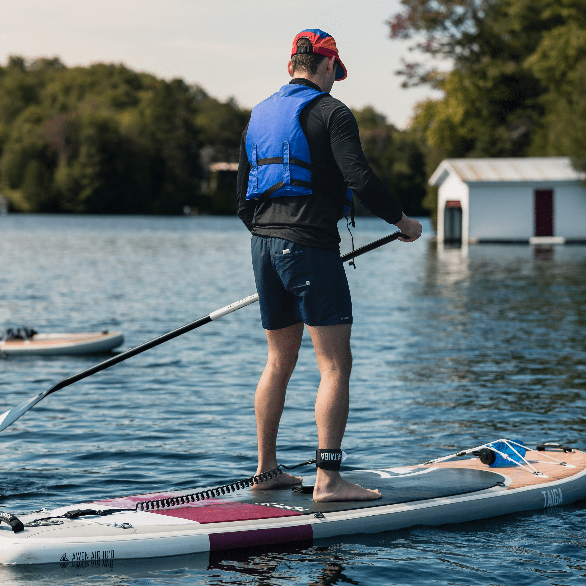 Planche SUP gonflable Awen 10'0'' Taiga Board, couleur bourgogne, mise en contexte avec homme qui pagaie sur un lac, détail leash avec logo Taiga